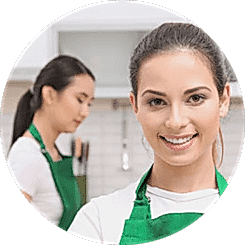 Two women in aprons are smiling for the camera.
